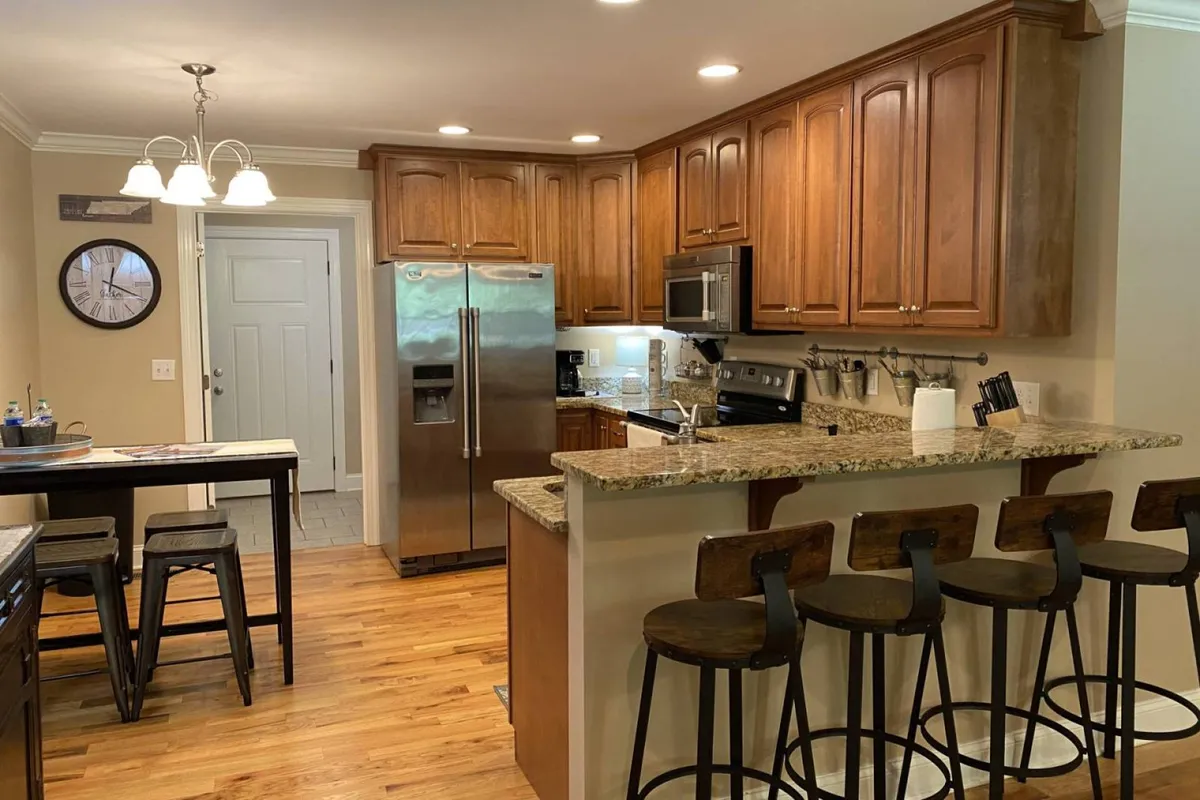 A spacious kitchen with a granite countertop, wooden cabinetry, stainless steel appliances, and bar stools. The layout encourages cooking, entertaining, and casual dining with family and friends.