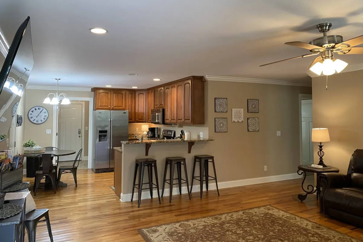 A cozy, open-plan kitchen with a large counter and bar stools seamlessly connects to a family living area, accentuated with wall art. The scene radiates warmth, inviting groups to cook, dine, and play games together after a day out.