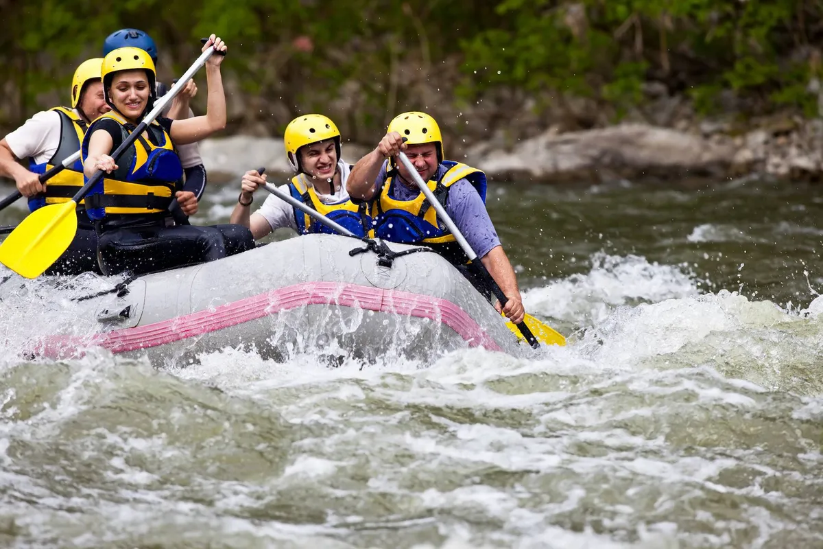 A group of people in a raft navigate white water rapids, all wearing helmets and wielding paddles. The scene is energetic and vibrant, capturing the thrill and camaraderie of outdoor adventure sports.