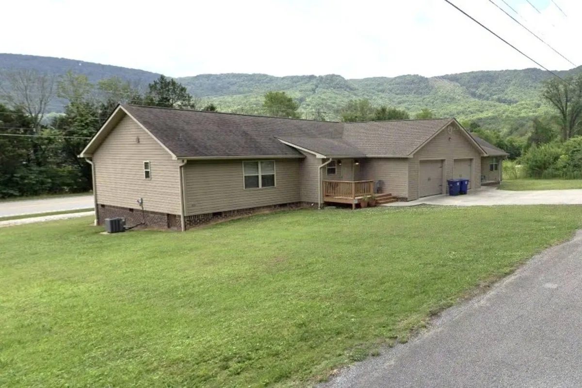 A welcoming exterior shot of the house with a clear view of the front porch, set against the backdrop of mountains. The yard is spacious and inviting, ideal for groups to gather before or after an event. The image evokes a sense of arrival and highlights the close proximity to local venues.