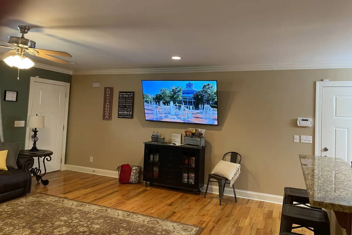 A comfortable living space with a sofa adorned with cushions, wooden flooring, a TV displaying a calming scene, and a black cabinet. The mood is perfect for family gatherings, movie nights, or simply relaxing after a fun day.