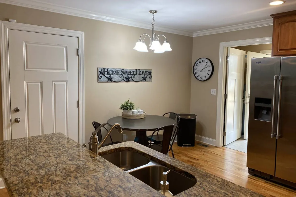 A cozy dining area adjoining the kitchen, featuring a granite countertop, an inviting dining table, home decor, and a stainless steel refrigerator. The space is styled for family meals and casual gatherings, emphasizing togetherness.