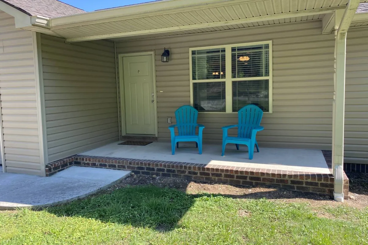 A close-up exterior view featuring blue chairs on the front porch, the front door, and a bright window. The setup invites guests to relax outdoors, socialize with friends or family, and enjoy the welcoming environment just outside their accommodations.