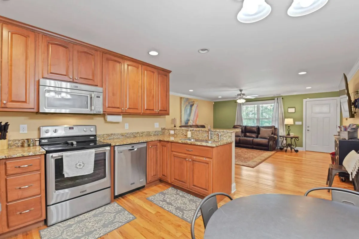 This image features a warm and welcoming kitchen with granite countertops, stainless steel appliances, wooden cabinetry, and a kitchen table. People can be seen cooking, gathering, and dining together, evoking a lively and communal atmosphere.