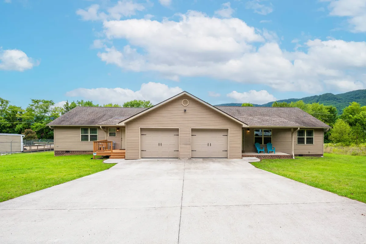The image shows the welcoming exterior of a Chattanooga townhouse, featuring a sunny front porch with inviting blue chairs, double garage doors, and a neatly groomed lawn. The scene exudes a tranquil and friendly atmosphere, ideal for gatherings and relaxation.